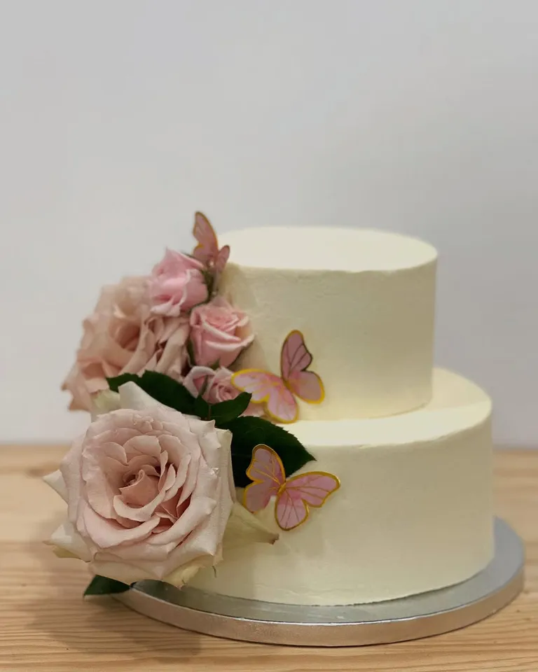 Tarta blanca de dos pisos con rosas y mariposas para una comunión
